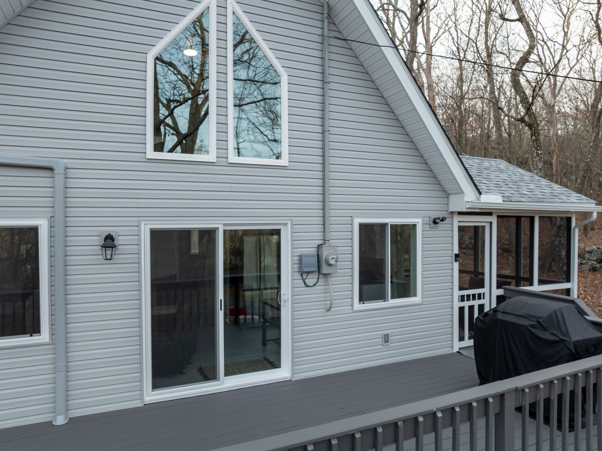 The back of a house with a screened in porch and a grill.