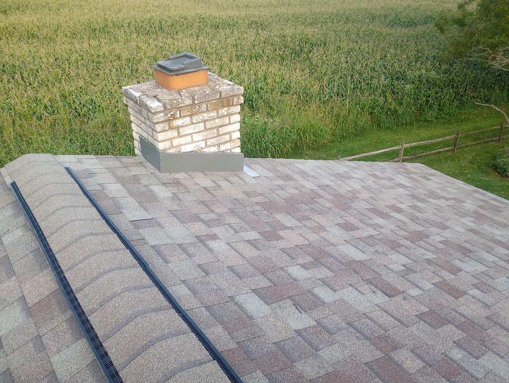 A chimney on top of a roof with a field in the background.