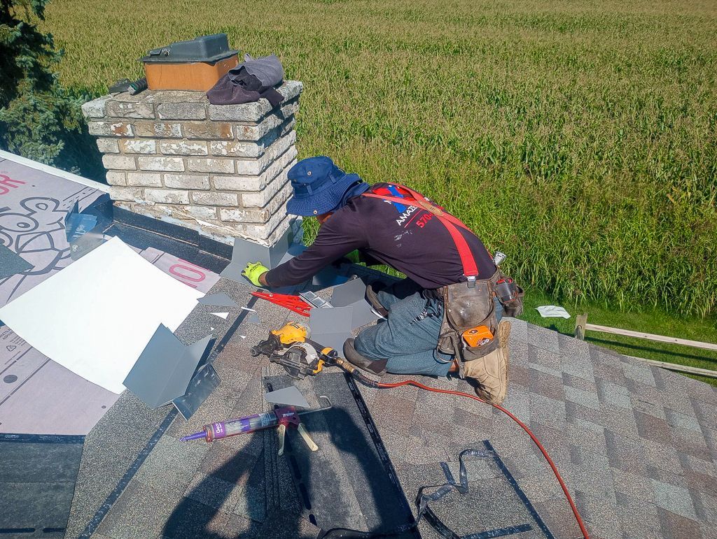 A man is kneeling on a roof working on a chimney.