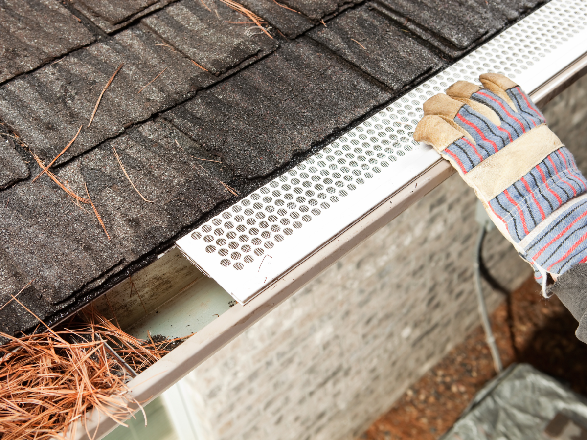 A person wearing gloves is cleaning a gutter on a roof.