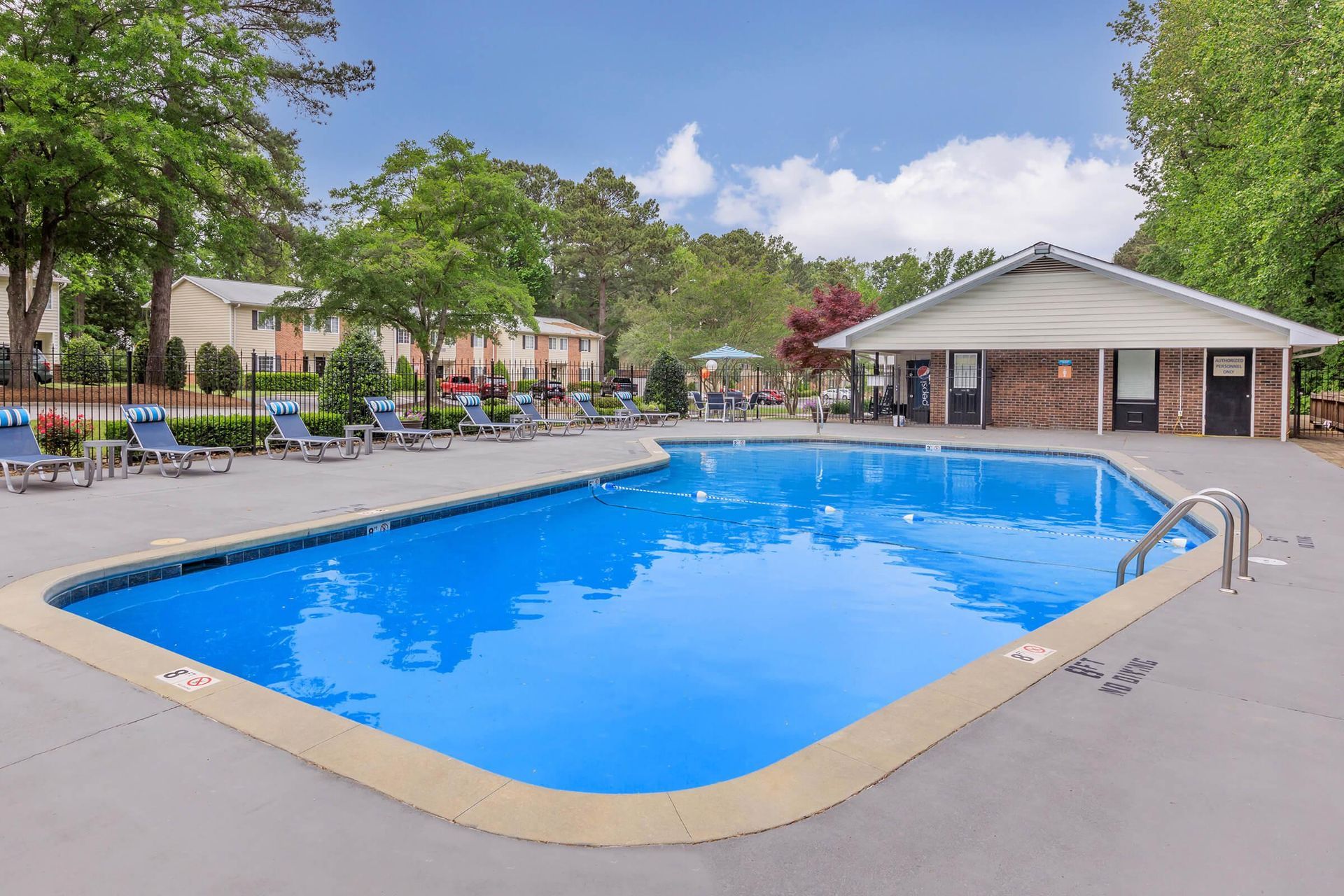 A large swimming pool is surrounded by chairs and a building.