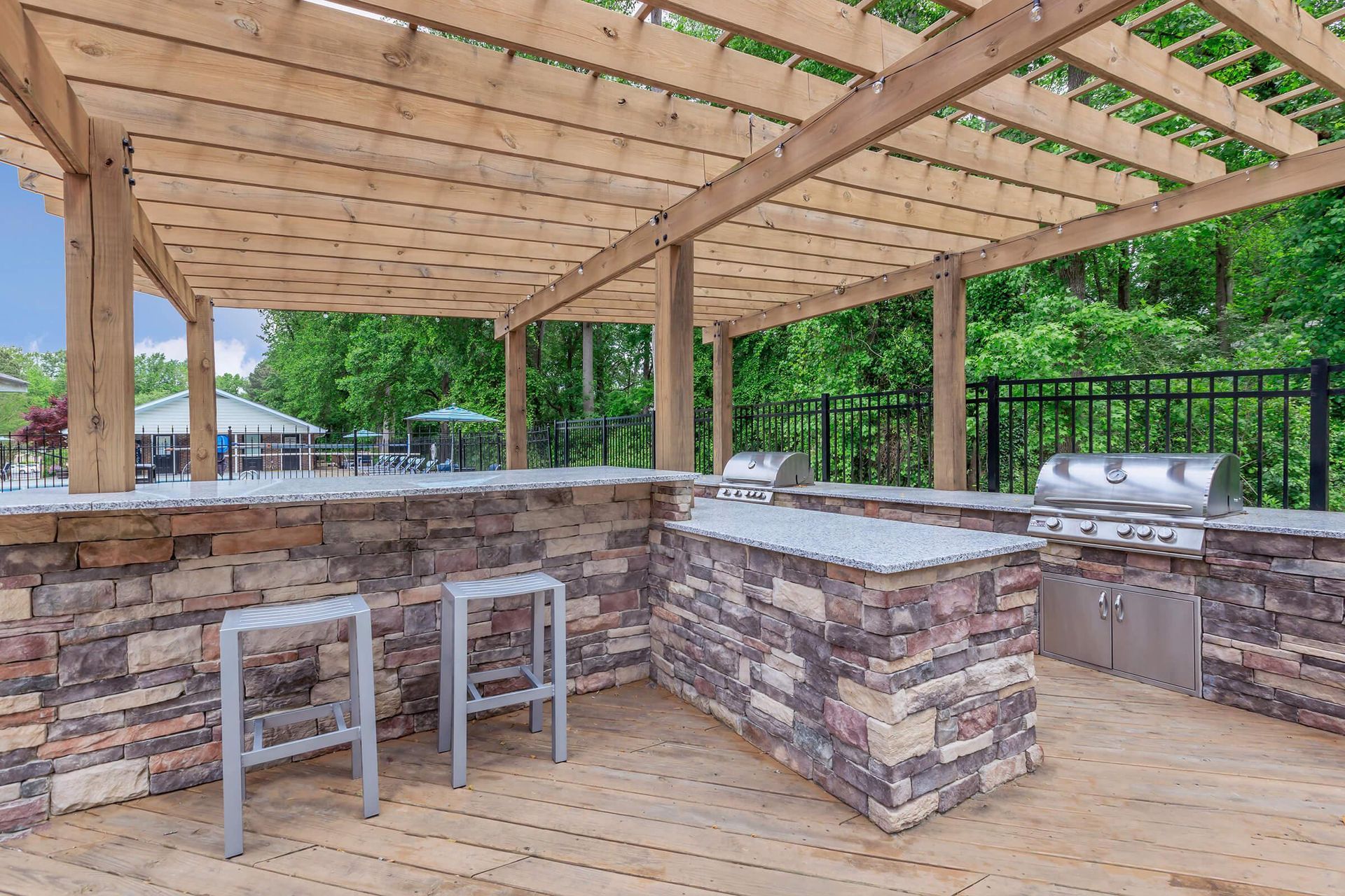 Outdoor kitchen with stone and wood elements, stainless steel grills, and seating area.