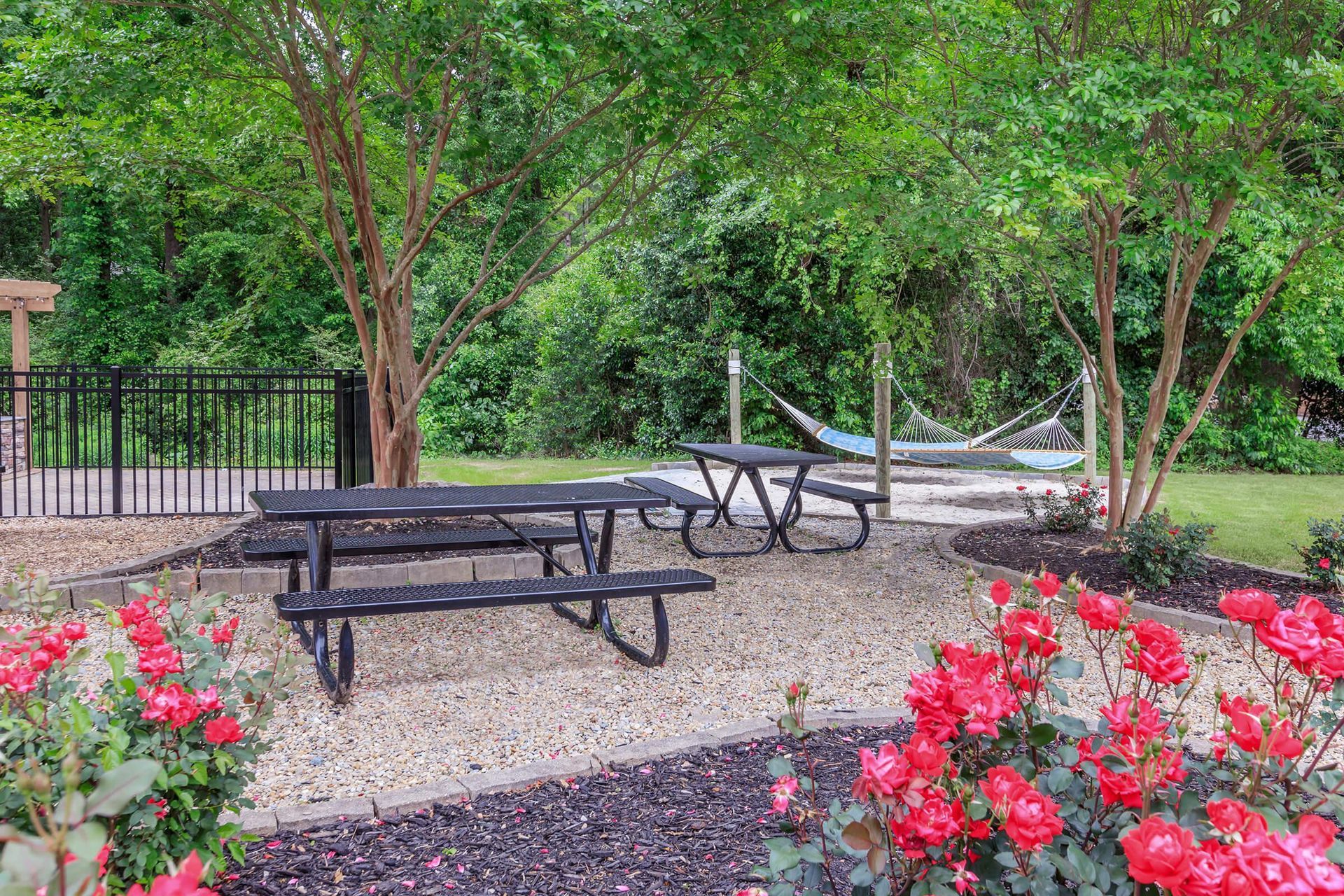 A picnic area with two picnic tables and a hammock surrounded by trees and flowers.