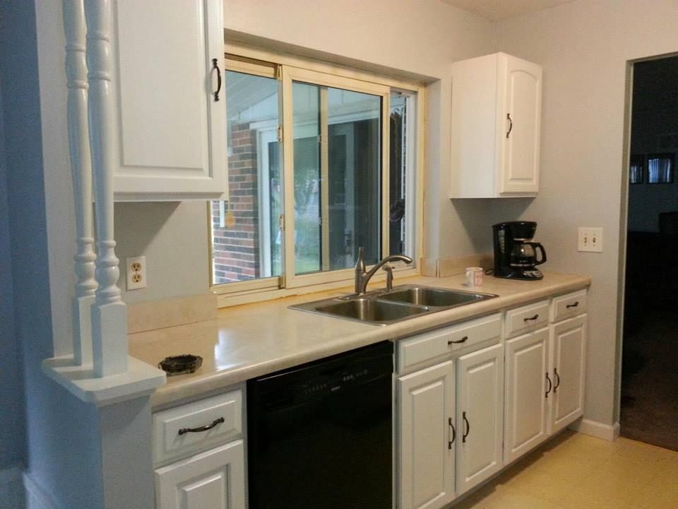 A kitchen with white cabinets , a sink , a dishwasher , and a window.