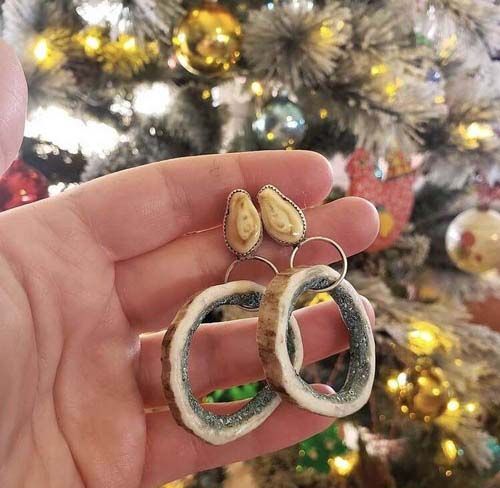A person is holding a pair of earrings in their hand in front of a christmas tree.