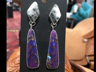 A pair of purple and white earrings are sitting on a black card.