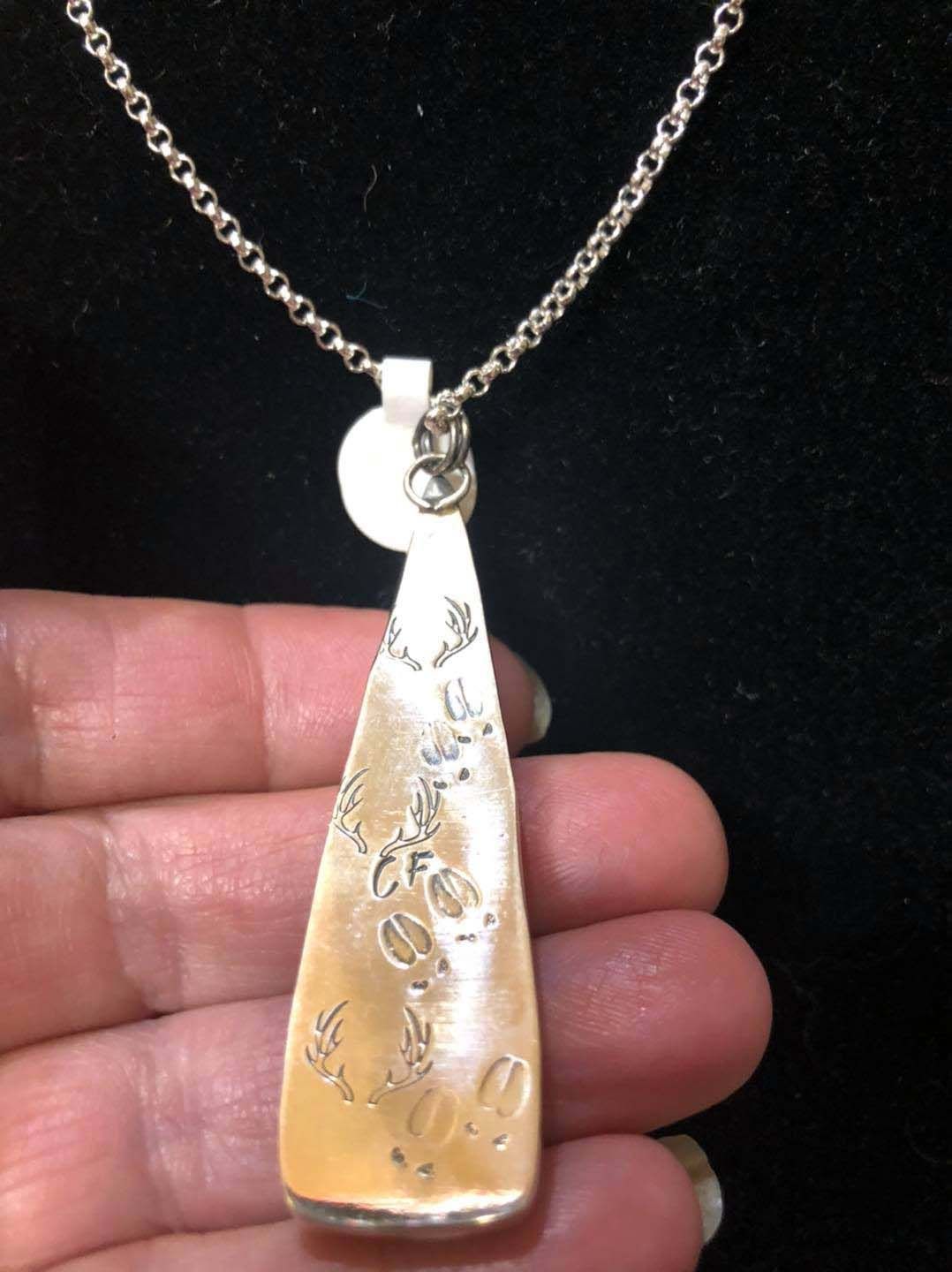 A person is holding a silver pendant on a chain