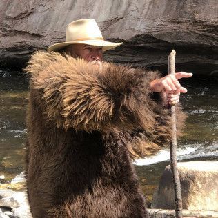 A man in a fur coat and hat is holding a stick.