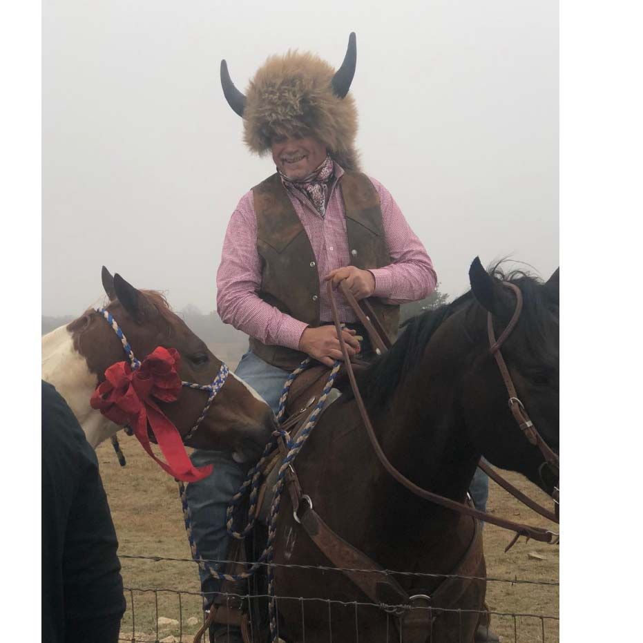 A man wearing a fur hat and horns is riding a horse