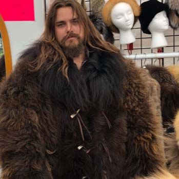 A man with long hair and a beard is wearing a fur coat