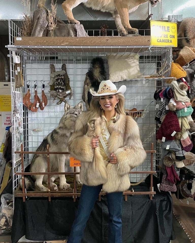 A woman in a fur coat is standing in front of a display of stuffed animals.