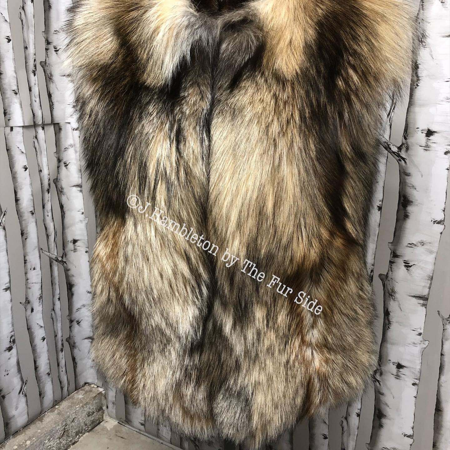 A fur vest is hanging on a wall in front of birch trees.