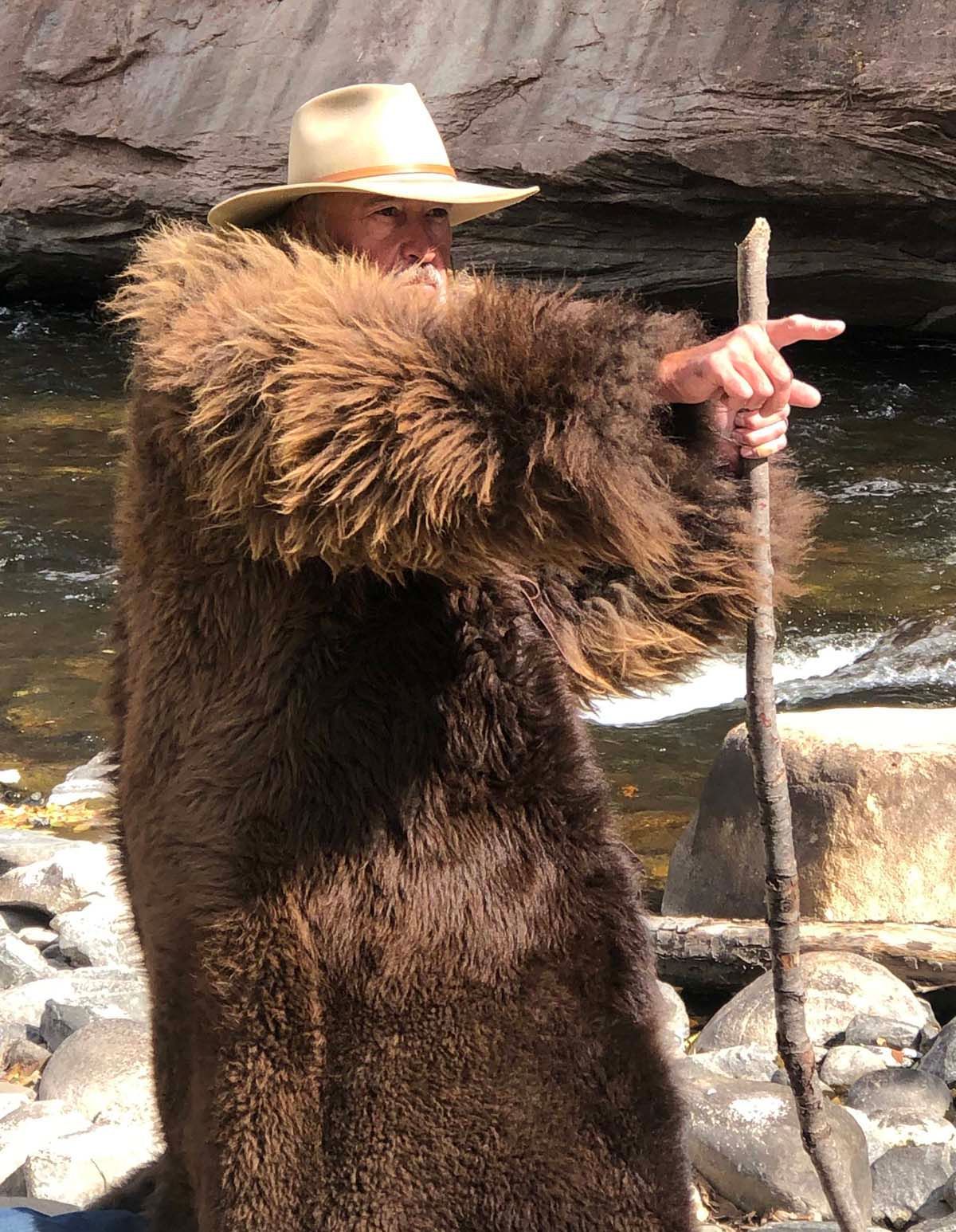 A man in a fur coat and cowboy hat is holding a stick.