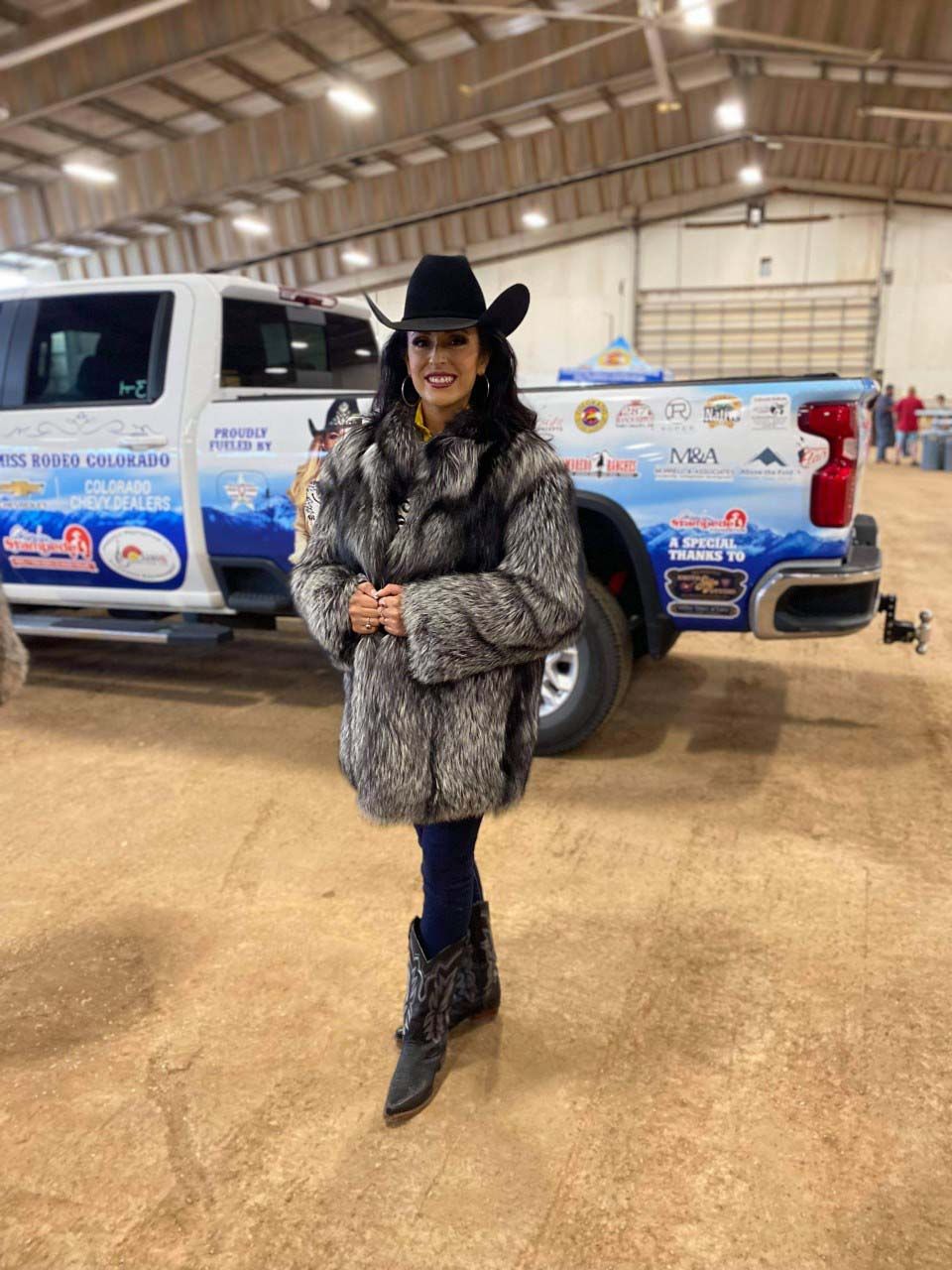 A woman in a fur coat and cowboy hat is standing in front of a truck.