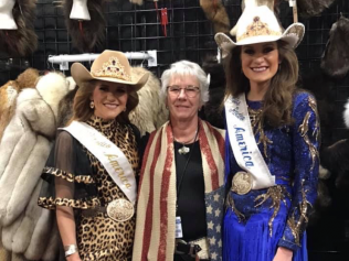 Three women are posing for a picture with one wearing a sash that says america