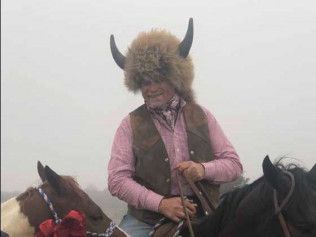 A man wearing a fur hat and horns is riding a horse.