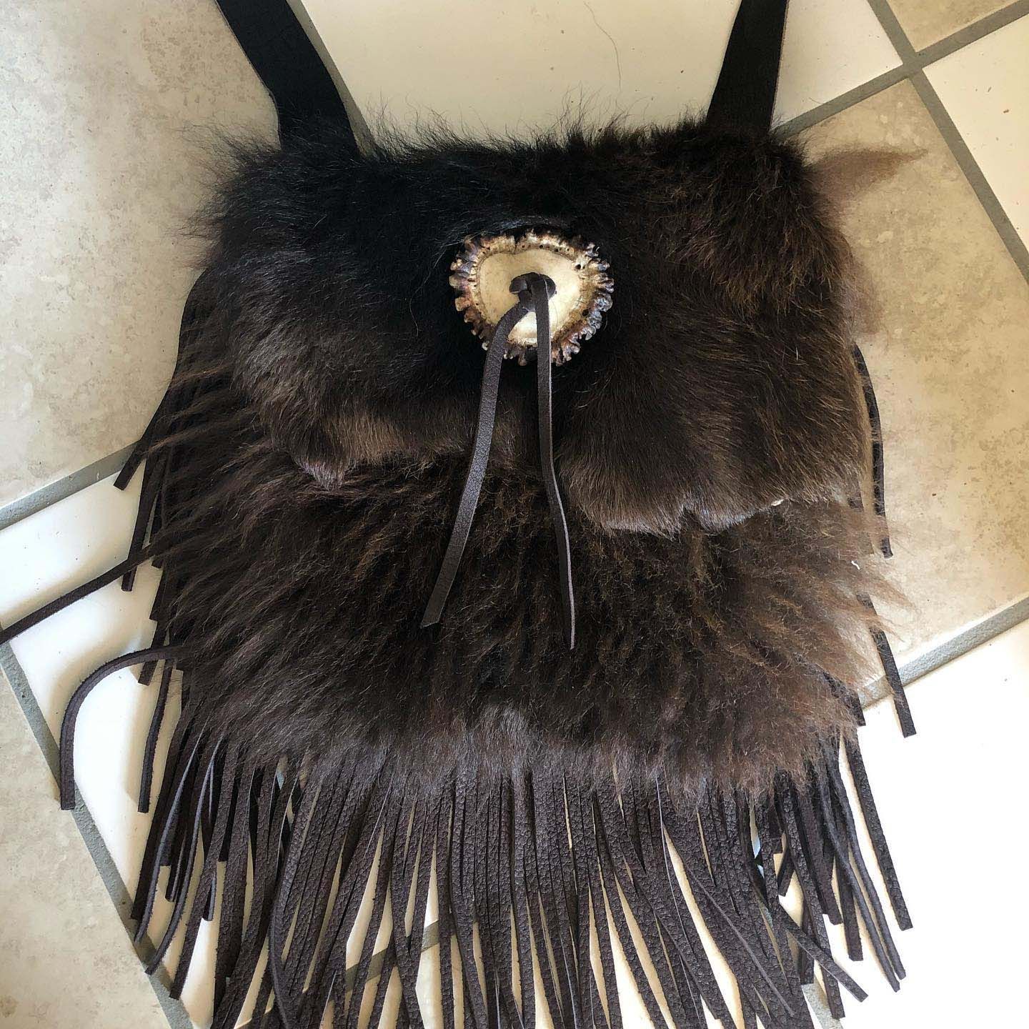 A brown furry purse with fringe is on a tiled floor