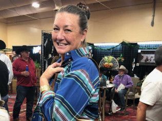 A woman in a blue plaid shirt is smiling in a crowded room.
