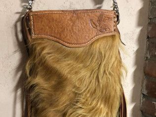 A purse made of fur and leather is hanging on a wall.