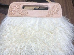 A white furry purse with a handle is sitting on a wooden table.