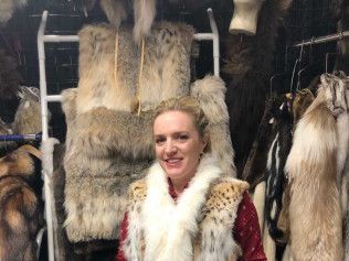 A woman wearing a fur vest is standing in front of a wall of furs.