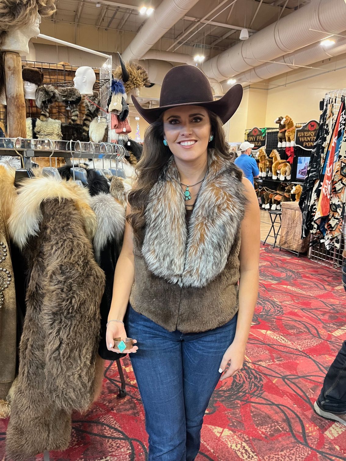 A woman in a fur coat and cowboy hat is standing in front of a mountain covered in snow.