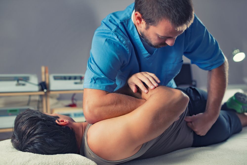 Chiropractor adjusting a patient's back on a massage table. The patient lies face down.