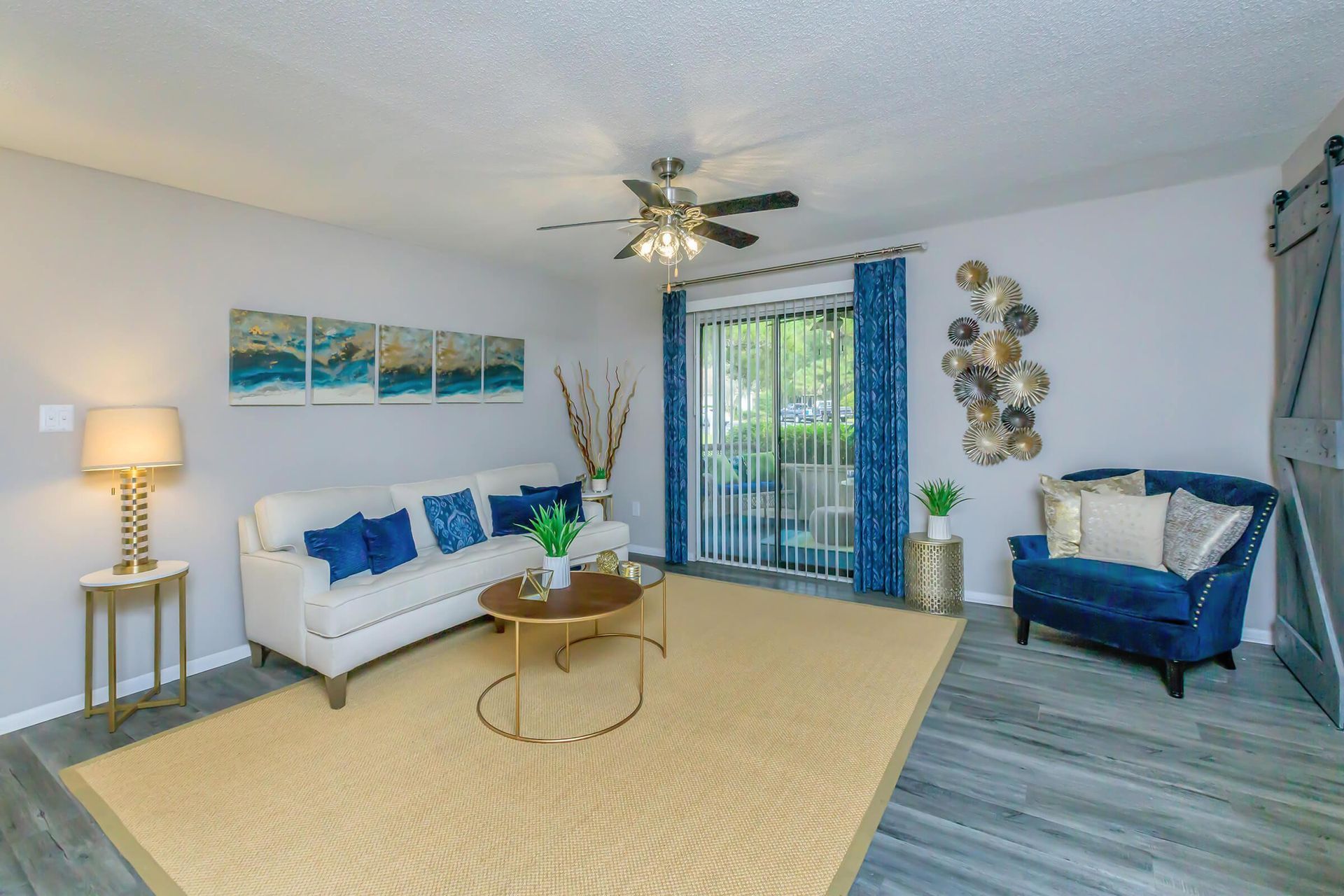 Spacious apartment iving room with sofa, rug, wall art, and ceiling fan at The Arbors.