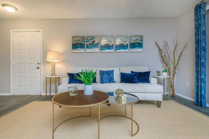 Living room with white couch, blue accents, and gold tables.