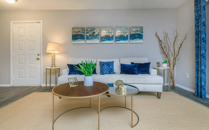 Living room with white couch, blue accents, and gold tables.