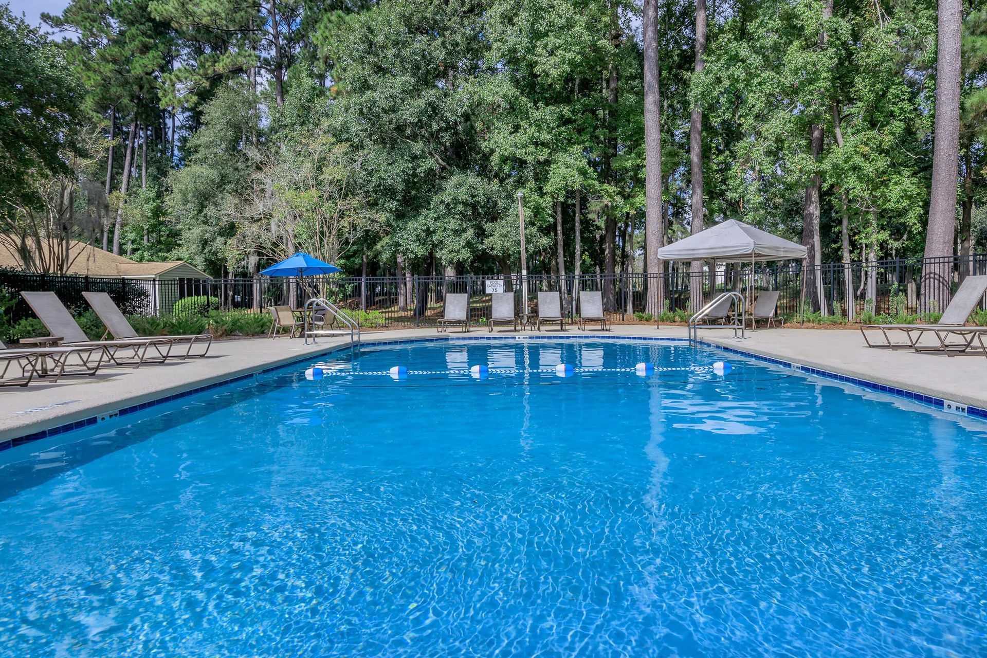 Swimming pool with lounge chairs, gazebo, and trees in the background.