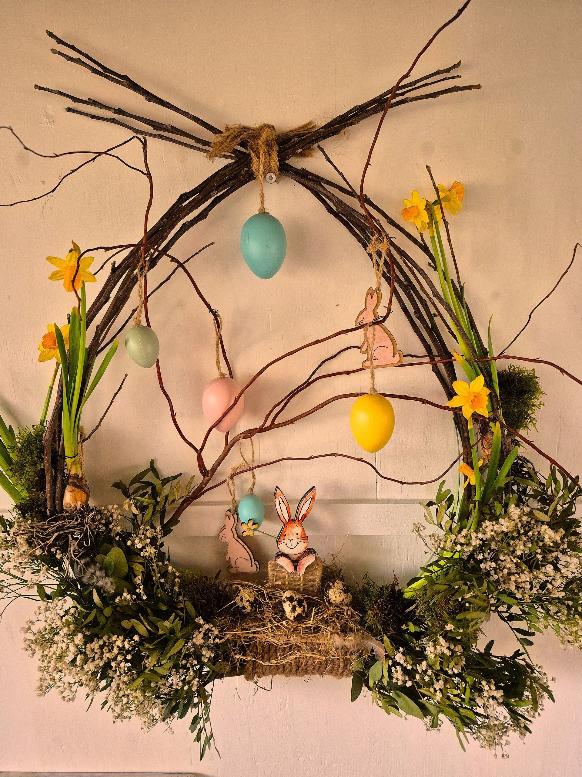 Decoratiefpaaskrans met kleurrijke eieren, takjes, mos en bloemen, hangend aan de muur.