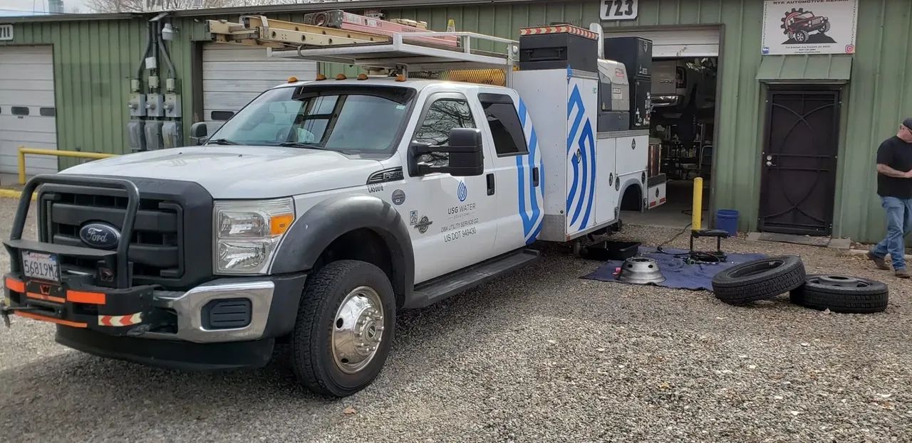 White Ford service truck with blue branding parked at a garage with tires removed for maintenance.