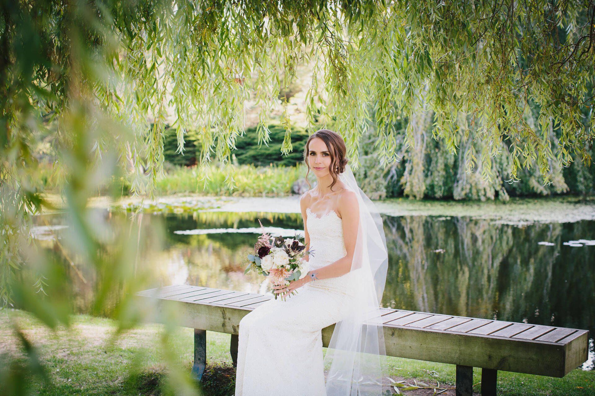 A Bride sitting on a bench by the lake