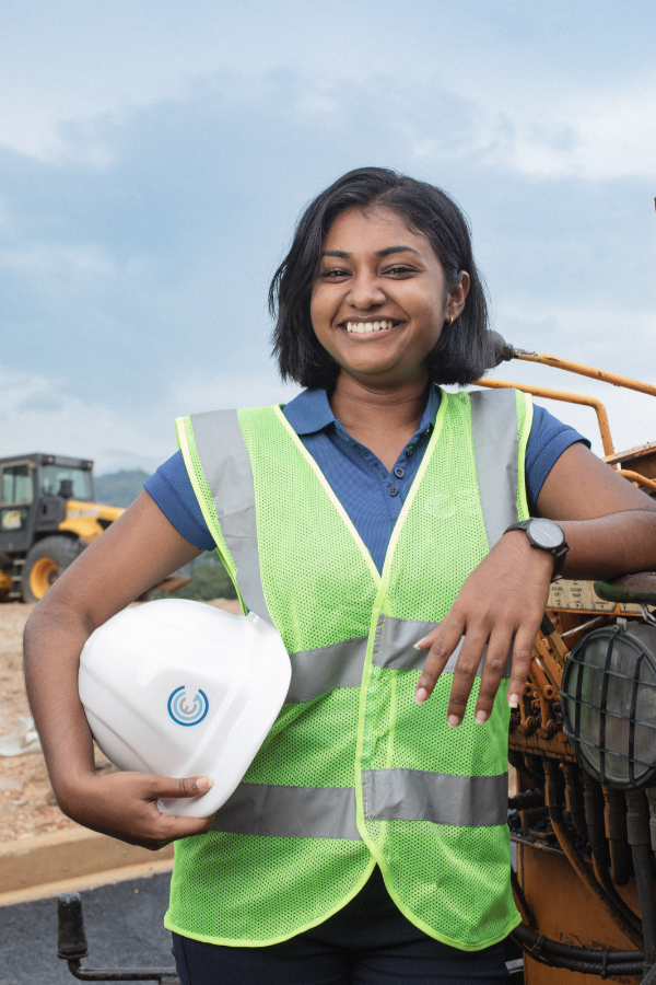 A woman in a safety vest is holding a hard hat and smiling.