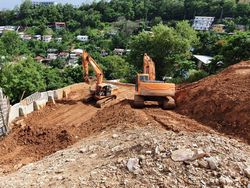 Two excavators are working on a dirt hill.