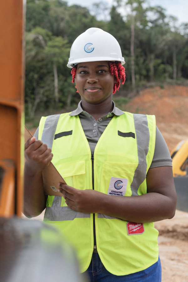 A woman wearing a hard hat and safety vest is holding a clipboard.