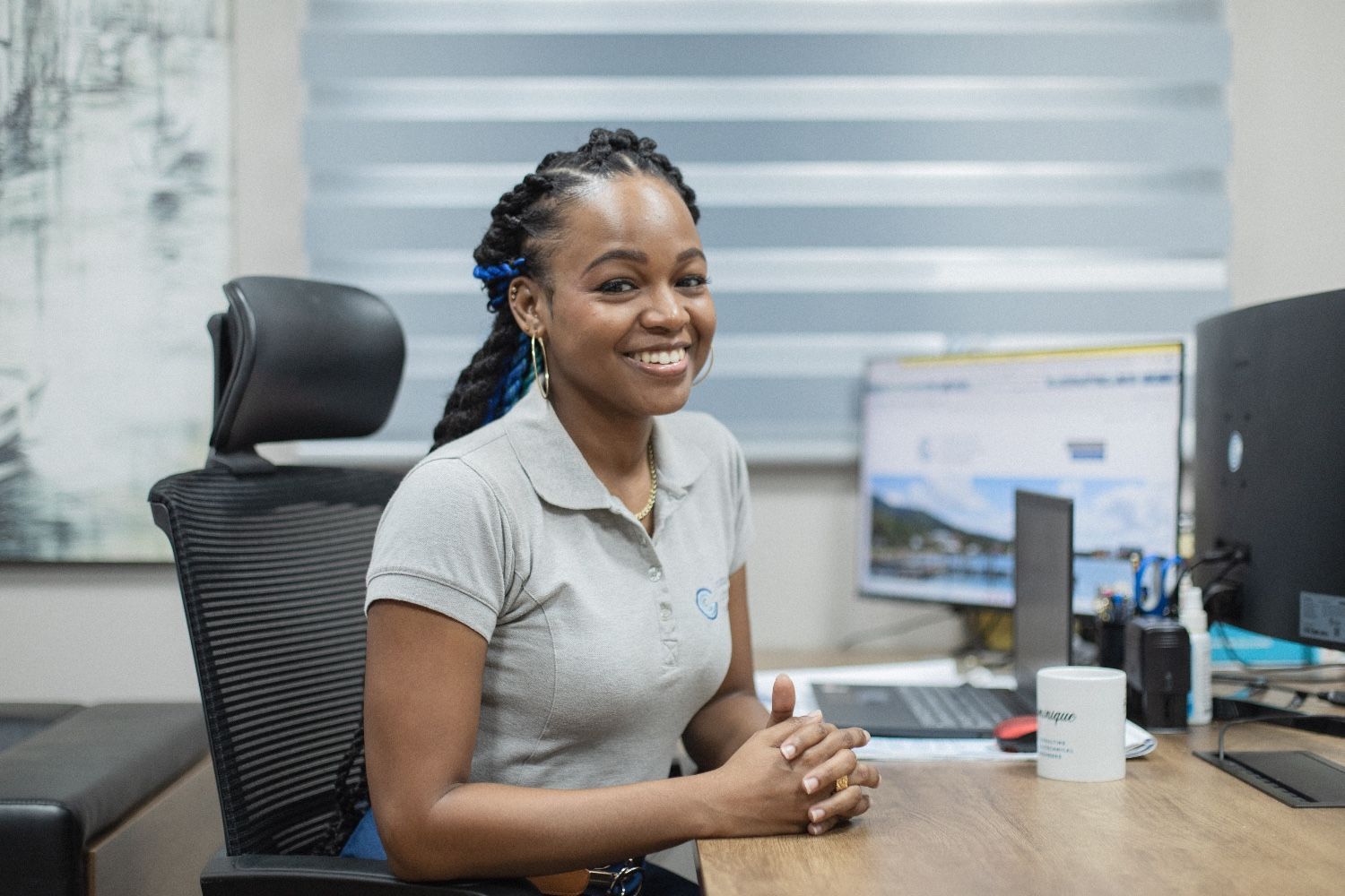 A woman is sitting at a desk in front of a computer and smiling.