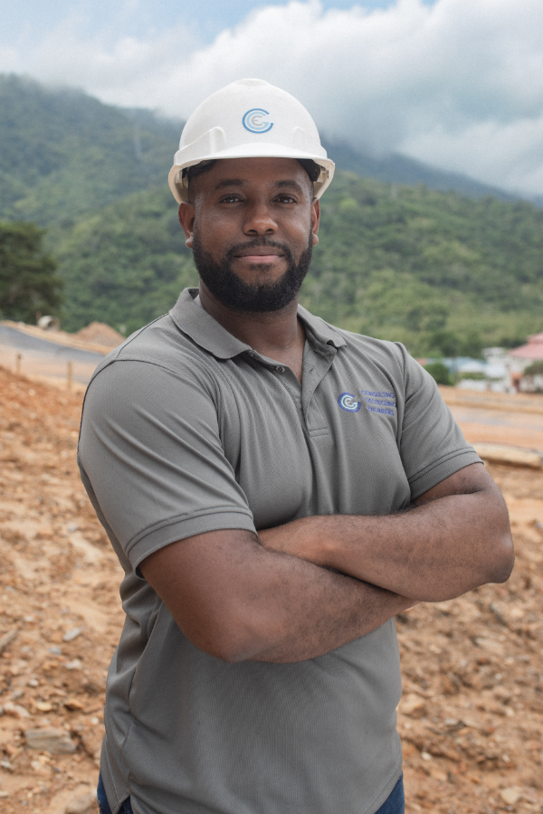 A man wearing a hard hat and a polo shirt is standing with his arms crossed.