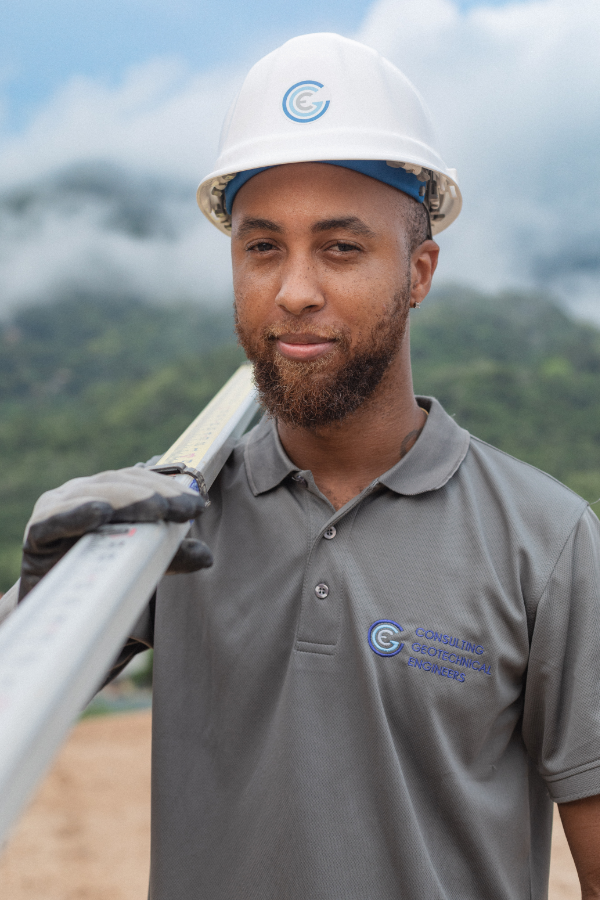A man wearing a hard hat and a gray shirt is holding a metal bar.