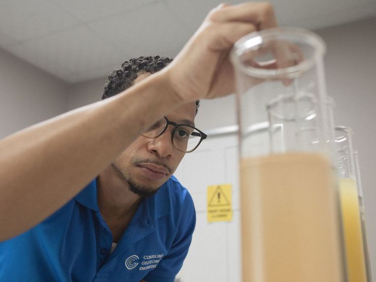 A man in a blue shirt is looking at a beaker of liquid.