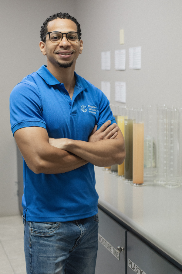 A man in a blue shirt is standing with his arms crossed in a lab.