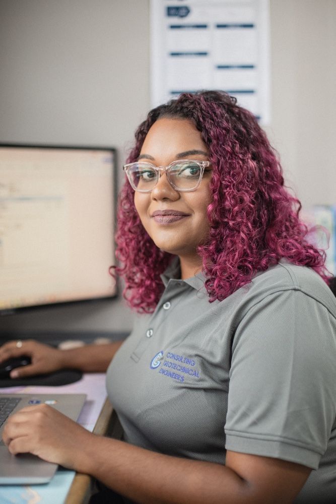 A woman with pink hair is sitting at a desk in front of a computer.
