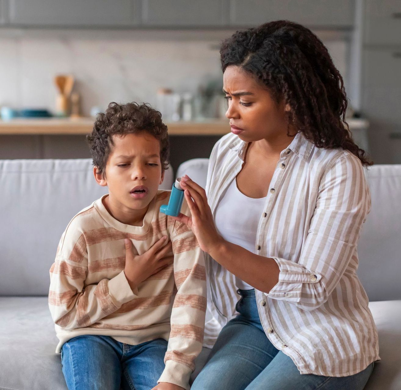 A woman is sitting on a couch with a child who is using an inhaler.