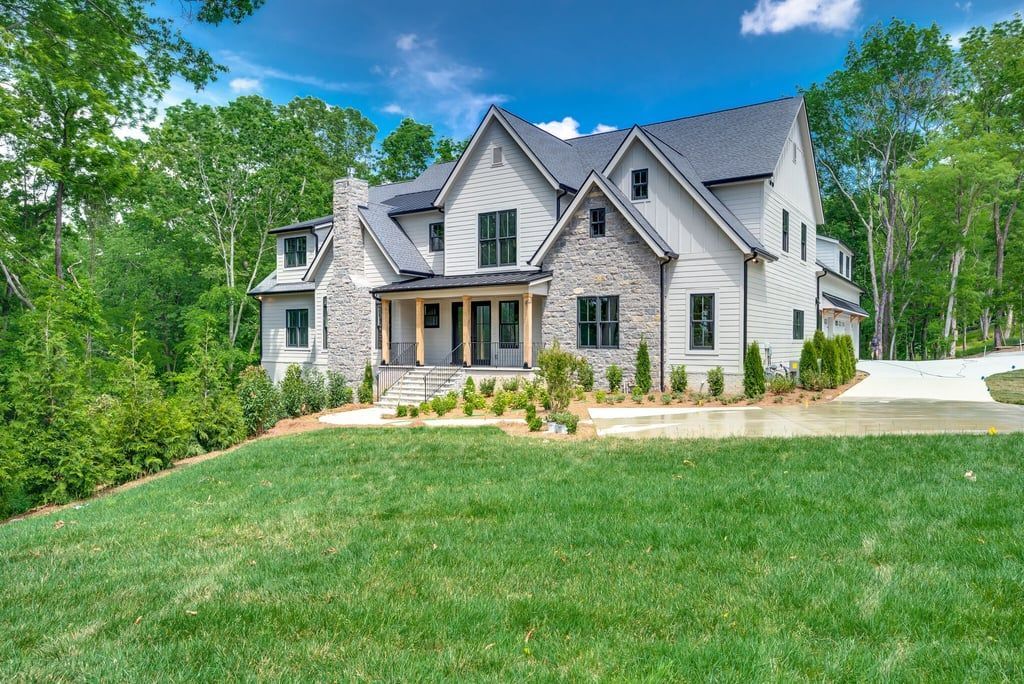 Two-story gray house with stone accents, surrounded by green lawn and trees.