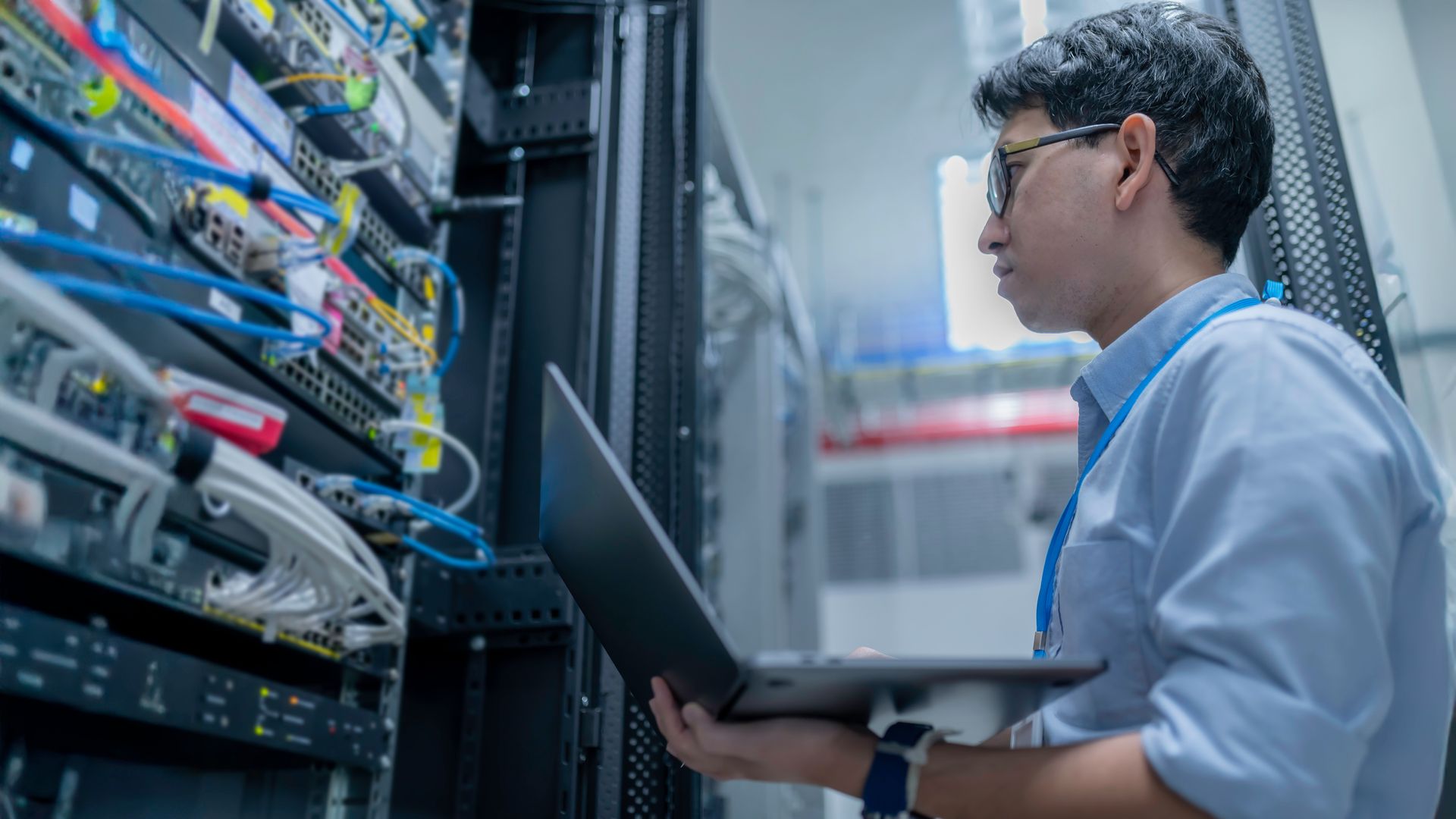 Person working on servers with a laptop in a server room.