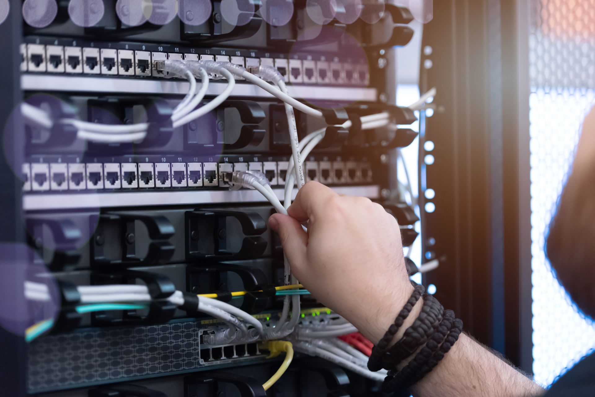 Person's hand adjusting network cables in a server rack, with various colored wires and connectors.