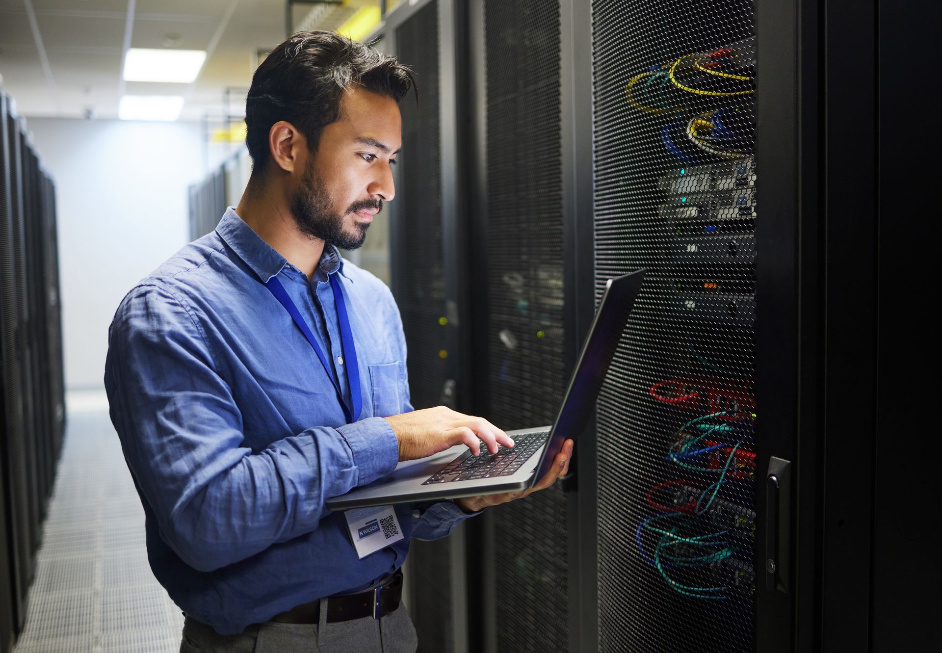 Technician using a laptop, inspecting servers in a data center.