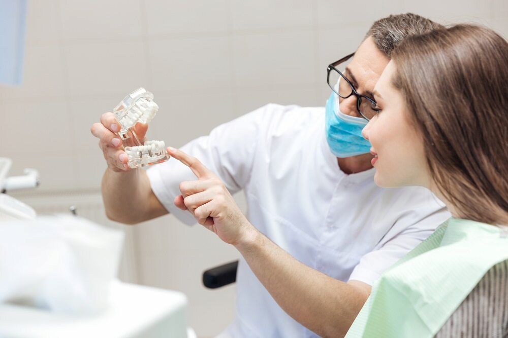 A Dentist Is Showing A Model Of A Tooth To A Patient — Highlands Denture Clinic in Willow Vale, NSW