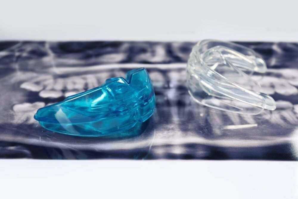 Two mouth Guards are Sitting on top of an x-ray of a Person 's Teeth — Highlands Denture Clinic in Willow Vale, NSW
